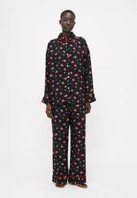 Musta pyjama-asusetti, jossa on punainen kukkakuosi, napitettava paita, jossa on kaulus, ja löysät housut, joissa on erottuvat helmakoristeet.