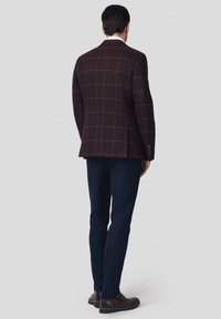 Brązowa marynarka w kratę o dopasowanym kroju, w zestawieniu z ciemnonawowym spodniami i brązowymi skórzanymi butami, widok od tyłu.