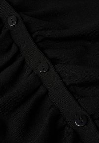Tissu tricoté noir avec une rangée de petits boutons noirs et des détails froncés le long de la bande de boutons.