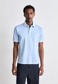 Polo de cor azul clara com colarinho abotoado, mangas curtas e acabamento de colarinho contrastante. Feito de uma mistura de algodão suave.