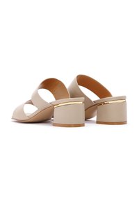 Mocassini beige open-toe con un design curvo e sezioni intagliate. Presentano un tacco spesso e liscio con un accento dorato attorno alla base.