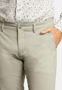 Chinos de color beige claro con una textura suave, que cuentan con un cierre de botón, lazos para cinturón y bolsillos laterales, complementados por una camisa de estampado en la parte superior.
