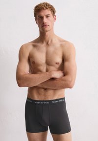 Boxers negros de tela suave; cuentan con una cinturilla de marca con el texto "Marc O’Polo"; diseño ajustado que resalta la forma del cuerpo.
