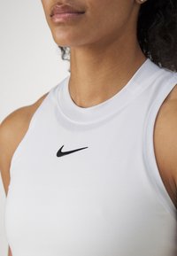 White athletic tank top featuring a high neckline, sleeveless design, and a black Nike logo on the chest. Smooth, stretchy fabric texture.