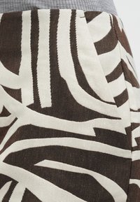 Prim-plan al unei țesături cu modele abstracte de frunze albe și maro închis și cusături vizibile la cusătură.