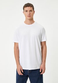 Hvid bomulds t-shirt med rund halsudskæring og korte ærmer, der har en glat tekstur og en afslappet pasform. Bæres med blå jeans.