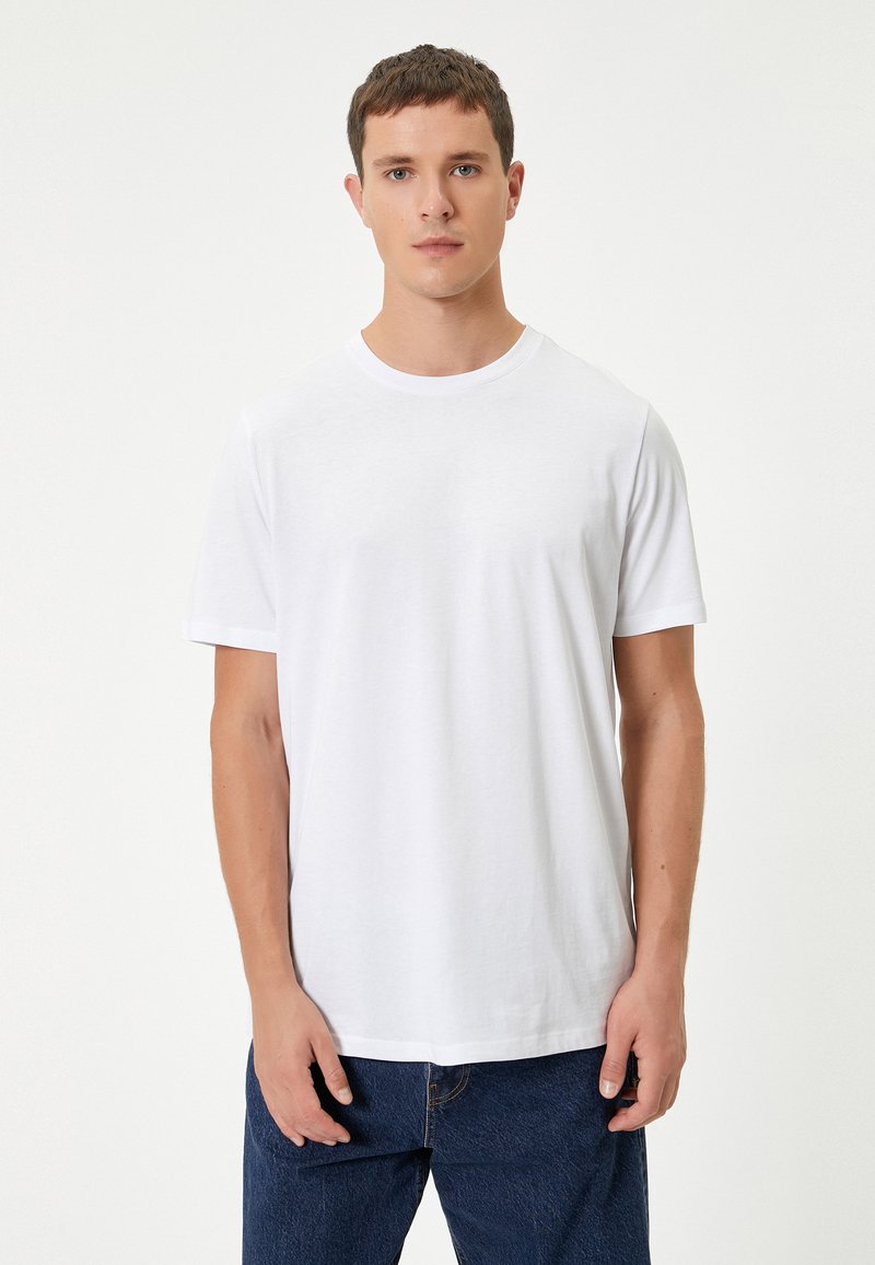 Hvid bomulds t-shirt med rund halsudskæring og korte ærmer, der har en glat tekstur og en afslappet pasform. Bæres med blå jeans.