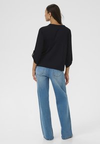 T-shirt noir à manches trois-quarts associé à un jean clair à jambes larges. Le haut présente un design simple et une texture lisse ; le jean a un lavage classique.