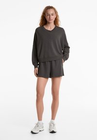 Mörkgrått matchande set med sweatshirt och shorts. Sweatshirten har en rund hals och knappdetalj; shortsen har elastisk midja. Passar för vardagsbruk.