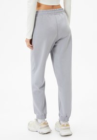 Pantalones de chándal gris claro con una cintura elástica, puños ajustados y textura suave, combinados con zapatillas blancas y beiges.