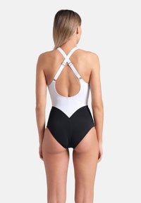 Maillot de bain une pièce avec un haut blanc et un bas noir. Il présente des bretelles croisées, un dos ouvert et un motif en chevrons à la taille.