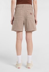 Pantalones cortos a rayas marrones y blancos con una cintura de altura media y dos bolsillos traseros. Fabricados con un material duradero, cuentan con un pequeño logotipo de la marca en la cinturilla.
