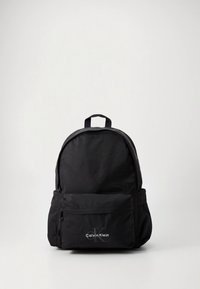 Mochila de tecido preto com parte superior arredondada, bolso frontal com fecho de correr e logótipo Calvin Klein em prata. Possui alças ajustáveis e uma pega resistente.