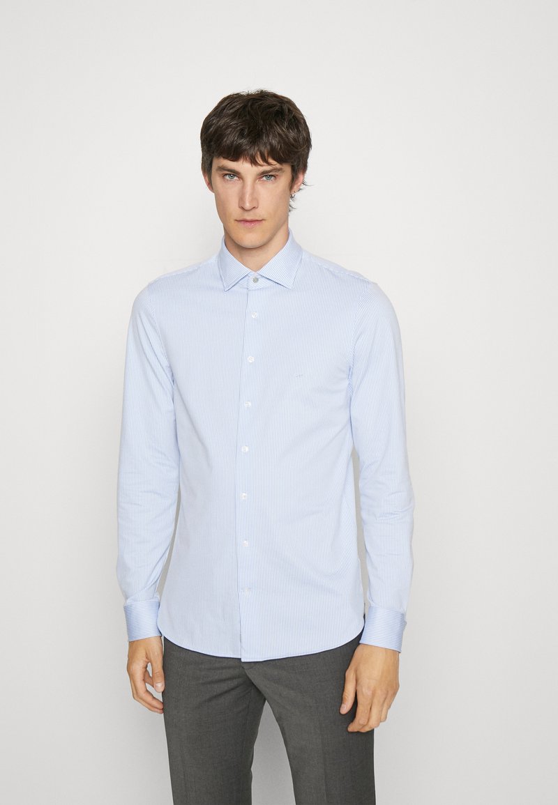 Hellblaues Button-Down-Hemd mit dünnen weißen Streifen, langen Ärmeln und einem Kentkragen, kombiniert mit grauen Hosen.