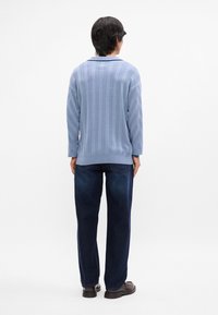 Pull en maille bleu clair avec des motifs côtelés verticaux et diagonaux, associé à un jean en denim foncé et des chaussures marron.