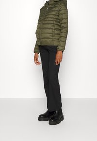 Oliwkowa, pikowana kurtka puchowa z zamkiem błyskawicznym i kapturem, w zestawieniu z czarnymi spodniami w dzwon oraz błyszczącymi czarnymi botkami na platformie.