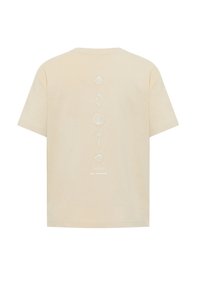 Beige cotton t-shirt with short sleeves, featuring white shell embroidery vertically along the center back and brand text at the bottom.