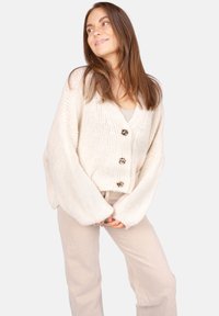 Off-white gestrickte Strickjacke mit V-Ausschnitt, langen Ärmeln und drei dekorativen Knöpfen an der Vorderseite. Weiche Textur, verkürztes Design.
