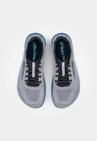 Baskets de course grises avec tiges en mesh, lacets noirs et semelle extérieure bleue. Comprend une semelle rembourrée et des détails accentués sur les côtés.