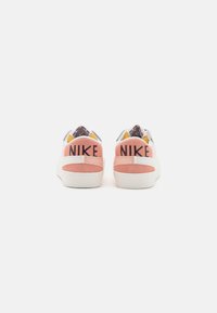 Nike-sneakers med en rosa mockaflik, vit mellansula och flerfärgade detaljer på ovandelen. Logotypen är tydligt visad på baksidan.