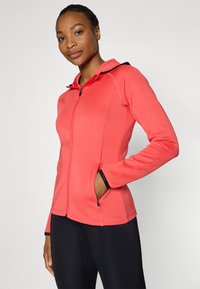 Korallfarvet zip-hoodie med hætte, lavet af strækbart stof. Har lynlåslommer og sorte detaljer på hætten og manchetterne.