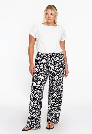 Weißes kurzärmliges Oberteil kombiniert mit weit geschnittenen, schwarz-weißen Hosen mit Blattdesign. Modell trägt flache Sandalen.