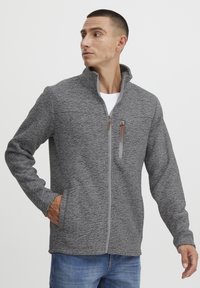 Giacca grigia con zip in tessuto testurizzato e colletto alto, caratterizzata da una zip frontale a contrasto e due tasche laterali. Vestibilità casual.