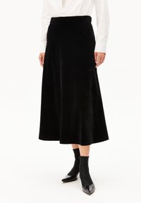 Schwarzer Midi-Rock aus einem weichen, strukturierten Stoff mit glattem Taillenumfang. Kombiniert mit enganliegenden schwarzen Stiefeletten und einem weißen Hemd mit Knöpfen.