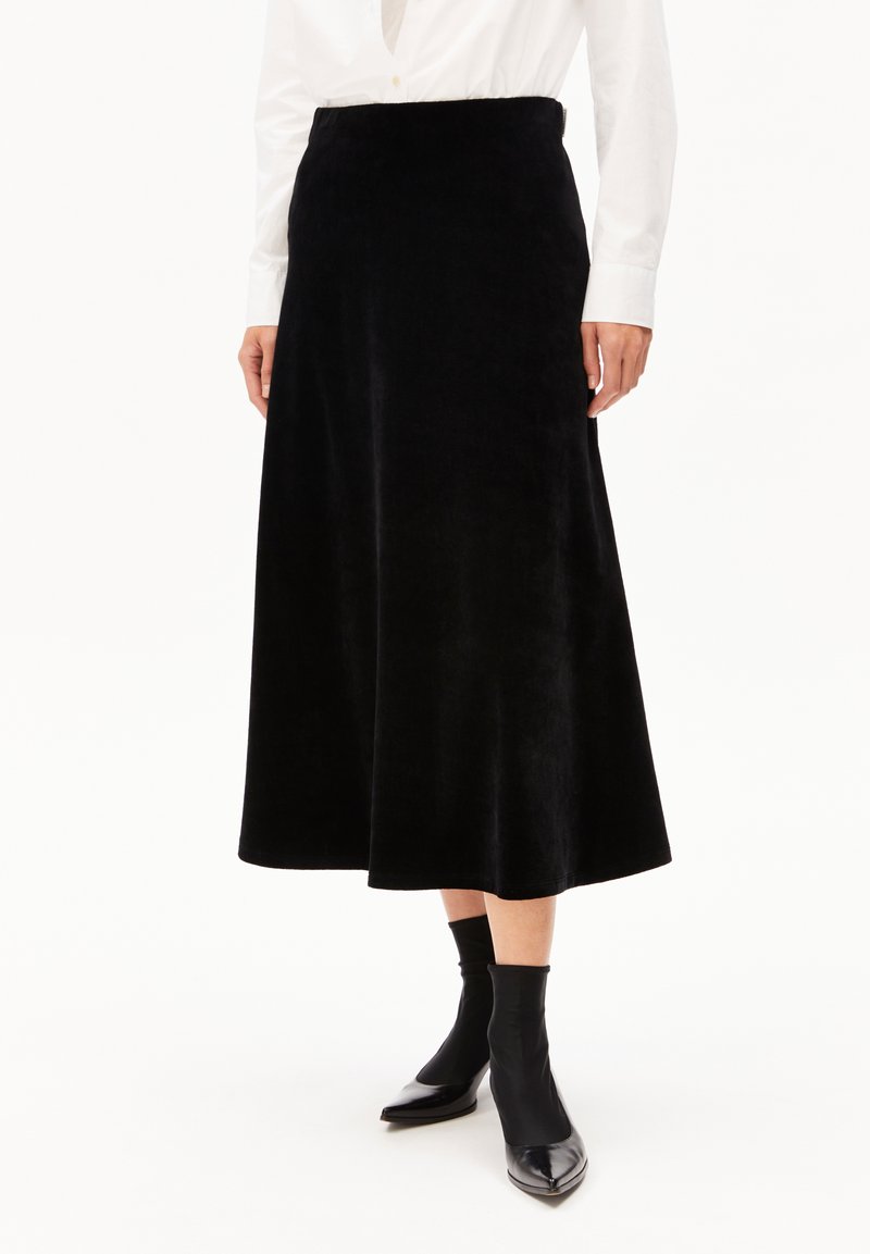 Schwarzer Midi-Rock aus einem weichen, strukturierten Stoff mit glattem Taillenumfang. Kombiniert mit enganliegenden schwarzen Stiefeletten und einem weißen Hemd mit Knöpfen.