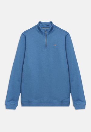 Blå langærmet pullover med halv lynlås og lille broderet logo på venstre bryst, ribstrikkede manchetter og kant.