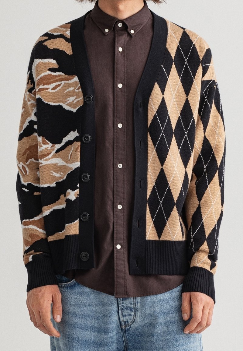 Stickad cardigan i nyanser av svart, beige och vitt med ett abstrakt mönster på ena sidan och rutig design på den andra; knappstängning.