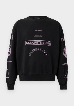 Fekete pulóver rózsaszín felirattal, beleértve a "CONCRETE BORN" és "UNBREAKABLE" szavakat, valamint a hüvelyeken található arcokkal és szimbólumokkal díszített grafikákat.