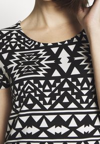 Haut à manches courtes noir et blanc avec un motif géométrique de triangles et de zigzags. Tissu en mélange de coton avec un col rond classique.