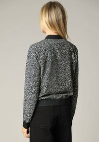 Zwarte bomberjack met wit abstract patroon, geribde manchetten en zoom, met een relaxte pasvorm en zachte stofstructuur.