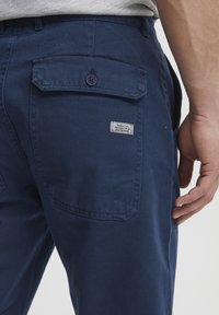 Pantalones azul marino con tejido texturizado, que cuentan con un bolsillo trasero con cierre de botón y una pequeña etiqueta cosida encima del bolsillo.