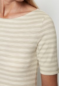 Krátký rukáv v béžové barvě s jemnými horizontálními pruhy, s lodičkovým výstřihem a měkkou strukturovanou látkou.
