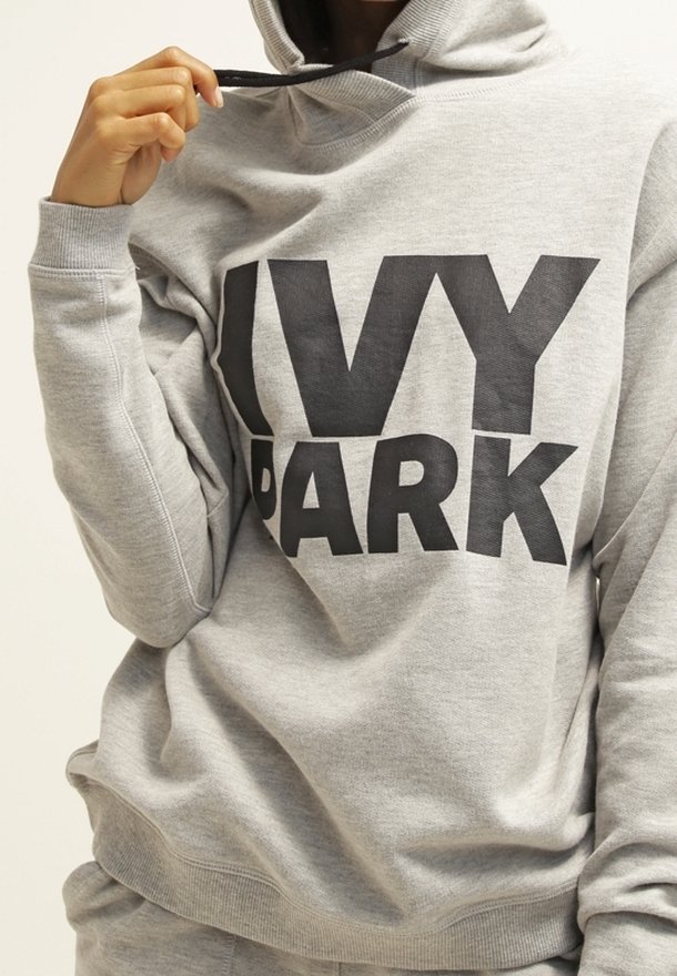 Szara bluza z kapturem z napisem "IVY PARK" w kolorze czarnym, wyposażona w sznurki przy kapturem i ściągacze przy rękawach. Miękka tekstura materiału; luźny krój.