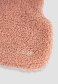 Tessuto di pile rosa con una superficie morbida e texturizzata. Presenta una forma arrotondata e un piccolo logo chiaro vicino al bordo.