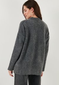 Cardigan gris texturé avec une coupe décontractée, des manches longues et un ourlet côtelé. Présente un col rond et un matériau doux et flou.