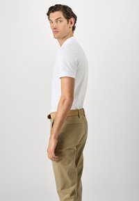Camisa polo blanca de manga corta, combinada con pantalones caqui y un cinturón marrón. La tela parece suave con un corte clásico.