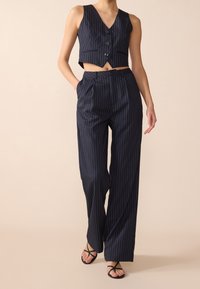 Navyrandig kort väst med knappar och höga randiga byxor. Lättviktig tyg med en mjuk textur och skräddarsydd passform.