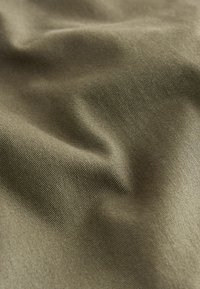 Tela de algodón en verde oliva con una textura suave, que presenta un sutil ribete diagonal y ligeros pliegues que crean una apariencia ondulada.