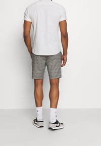 Camicetta grigia chiara a maniche corte con sottili righe, abbinata a pantaloni corti a quadretti grigi. Modello che indossa calze bianche e sneaker nero-grigie.