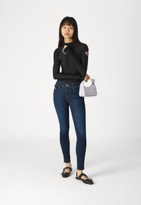 Μαύρη μπλούζα με μακριά μανίκια και κουκούλα, μπλε skinny τζιν, μαύρα επίπεδα παπούτσια με λεπτομέρεια από αγκράφα και μια μικρή γκρίζα τσάντα με χερούλι.