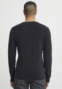 Pull en gris foncé avec une texture côtelée, des manches longues et un col rond. Design ajusté avec un ourlet droit et des fentes sur les côtés.