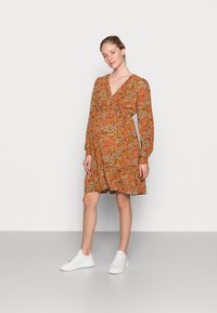 Vestido floral em tom rust, com decote em v, mangas longas e cintura ajustada por laço. Apresenta uma saia fluida e é combinado com ténis brancos.