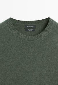 Grön kashmirtröja med rund halsringning. Har ribbstickade muddar och fåll. Etiketten innehåller varumärkesnamn och materialinformation.