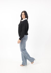 Maglione nero a maglia con una camicia bianca con colletto sotto, abbinato a jeans svasatiazzurri chiari e sandali con tacco trasparenti.