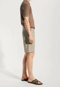 Braunes Poloshirt mit kurzen Ärmeln und Rippenstruktur, kombiniert mit hellbeigen Shorts und dunklen Sandalen, präsentiert eine entspannte Passform und einen lässigen Look.