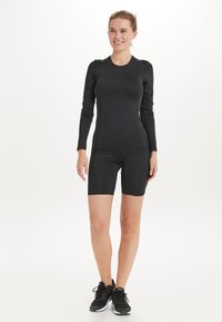 Schwarzes langärmliges Sportoberteil und passende Shorts aus einem glatten, dehnbaren Stoff. Das Design ist eng anliegend mit minimalen Nähten.